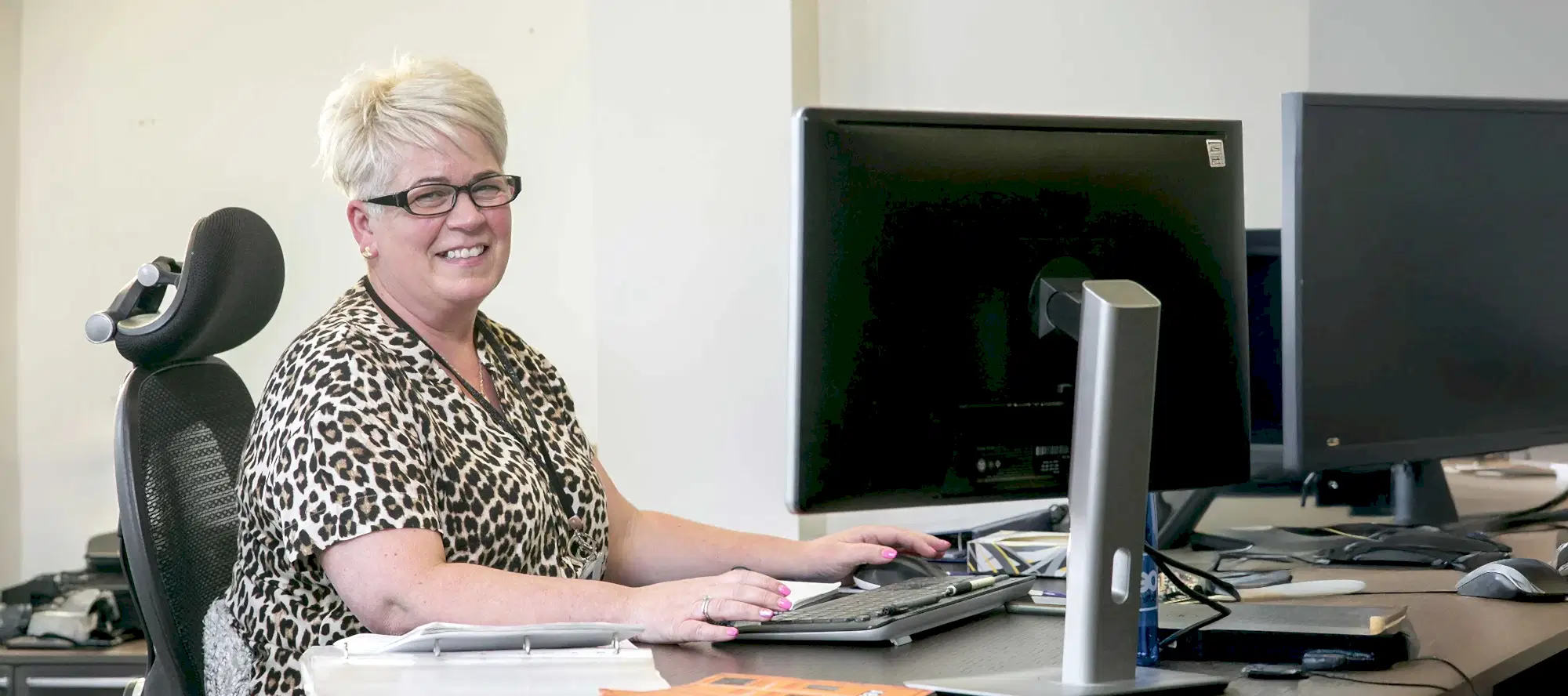 OEG certification administration assistant smiling at her desk.